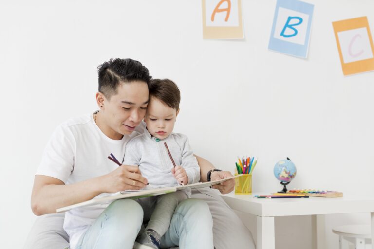 How ABA Therapy Supports Children With Autism in Singapore Father engaging in a home ABA therapy activity with his young child using coloring books and pencils, showcasing supportive learning for children with autism in Singapore.