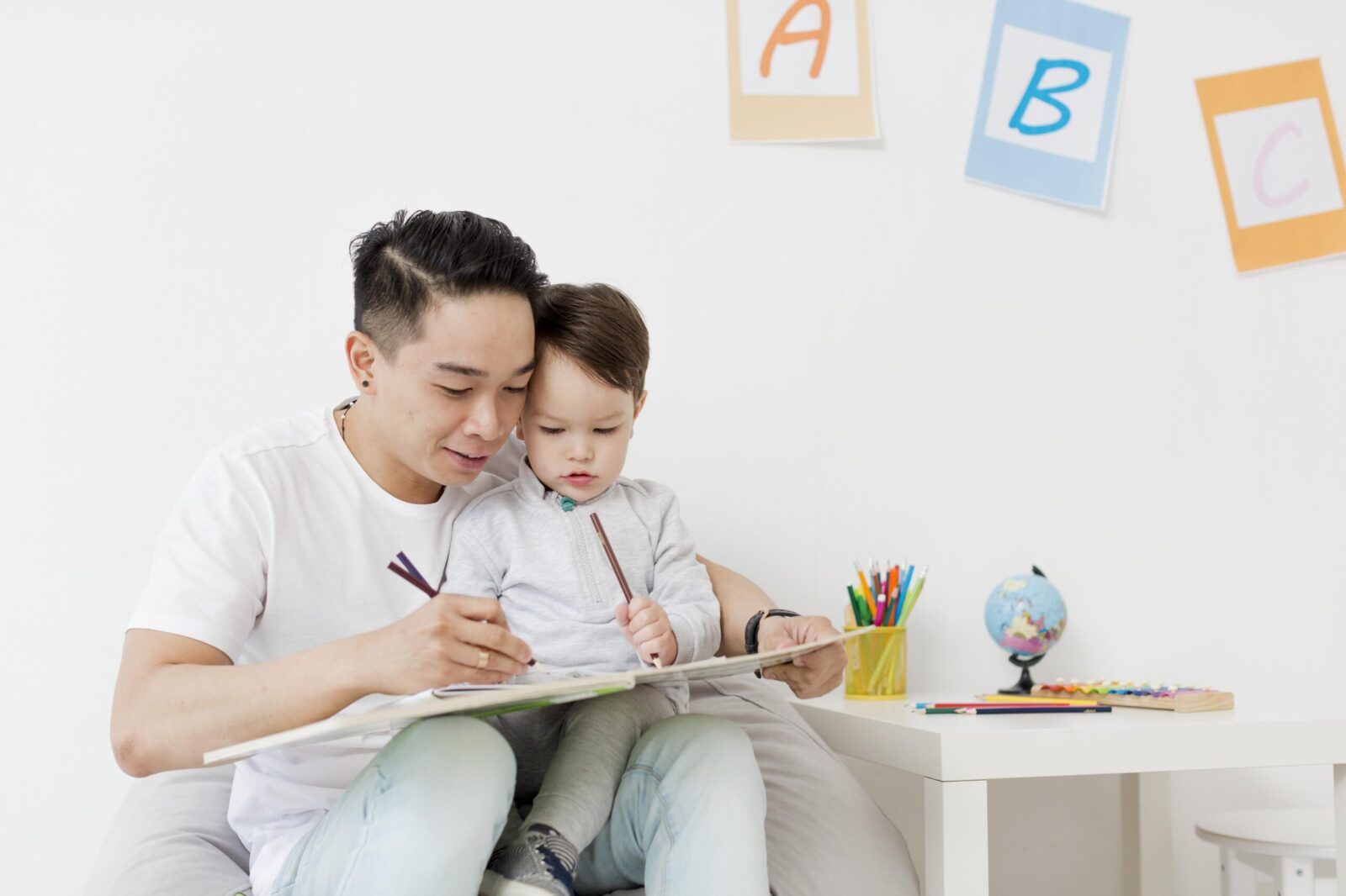 Father engaging in a home ABA therapy activity with his young child using coloring books and pencils, showcasing supportive learning for children with autism in Singapore.