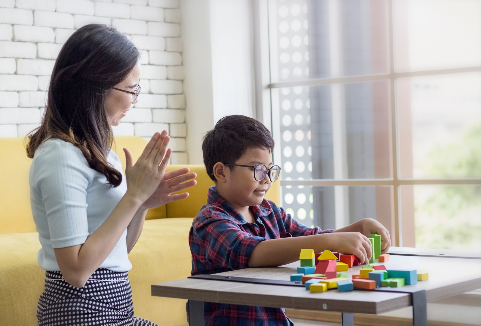 Therapist encouraging a young boy during a developmental therapy session with colorful blocks, addressing common misconceptions about autism therapy in Singapore.