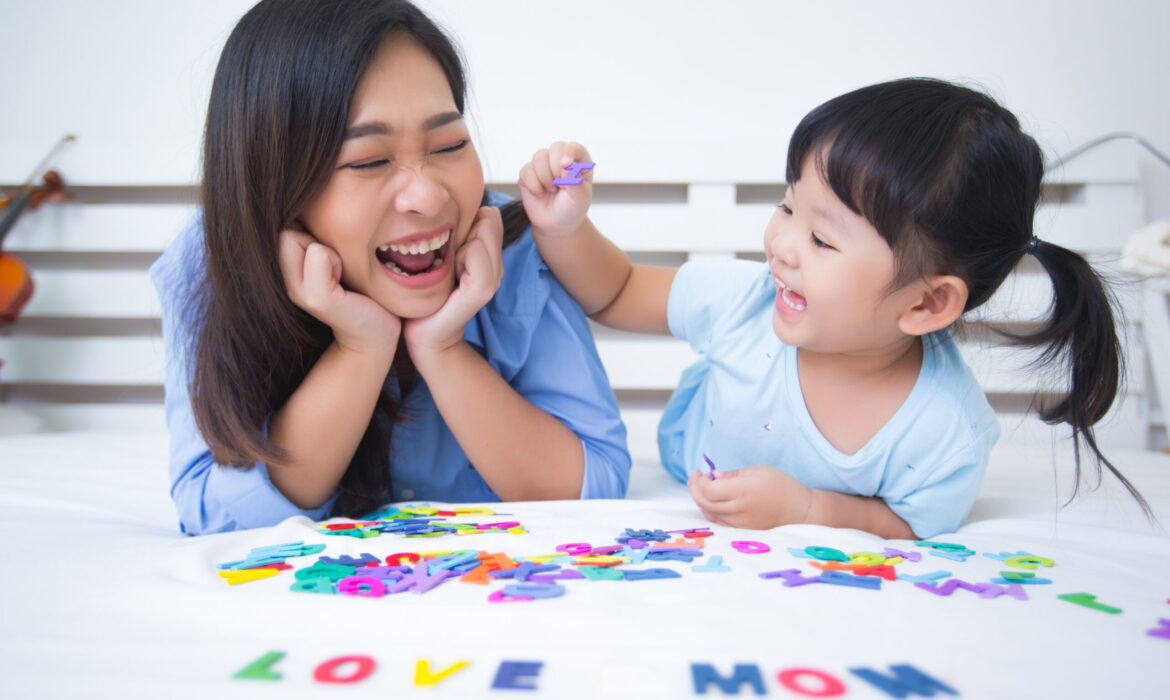 Mother and young daughter joyfully playing with colorful letters on a bed, illustrating the positive impact of ABA VB therapy in helping children develop speech and communication skills.