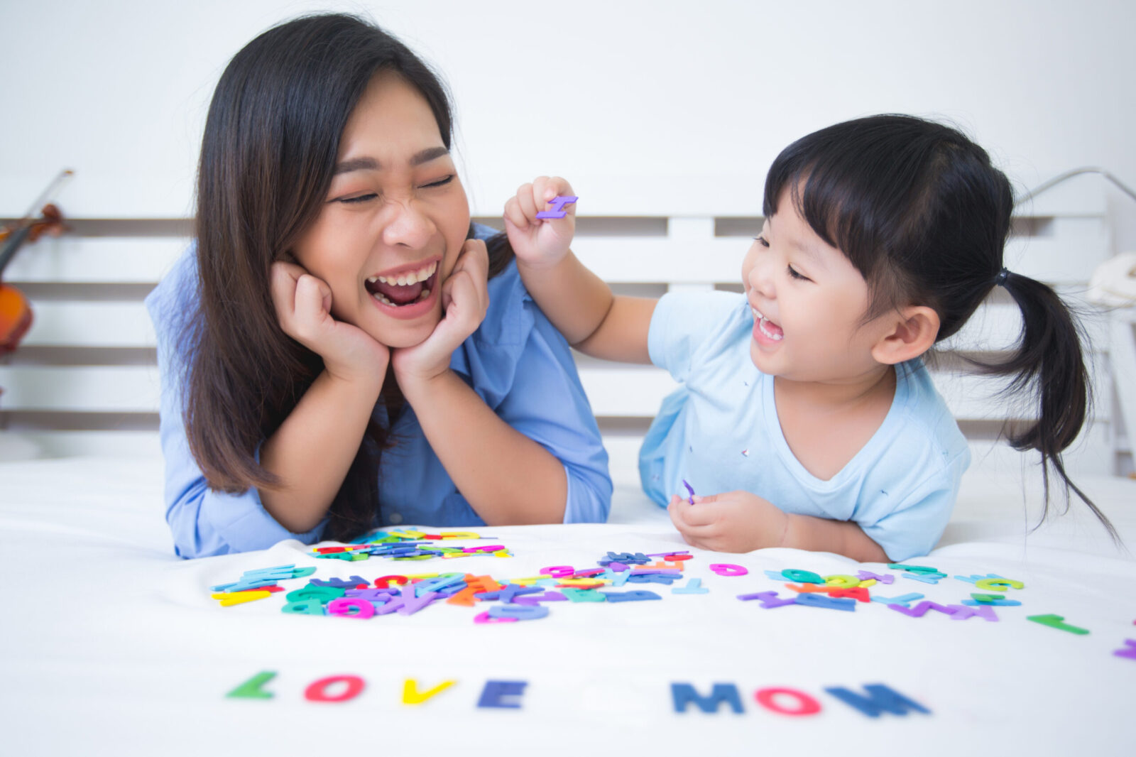 Mother and young daughter joyfully playing with colorful letters on a bed, illustrating the positive impact of ABA VB therapy in helping children develop speech and communication skills.