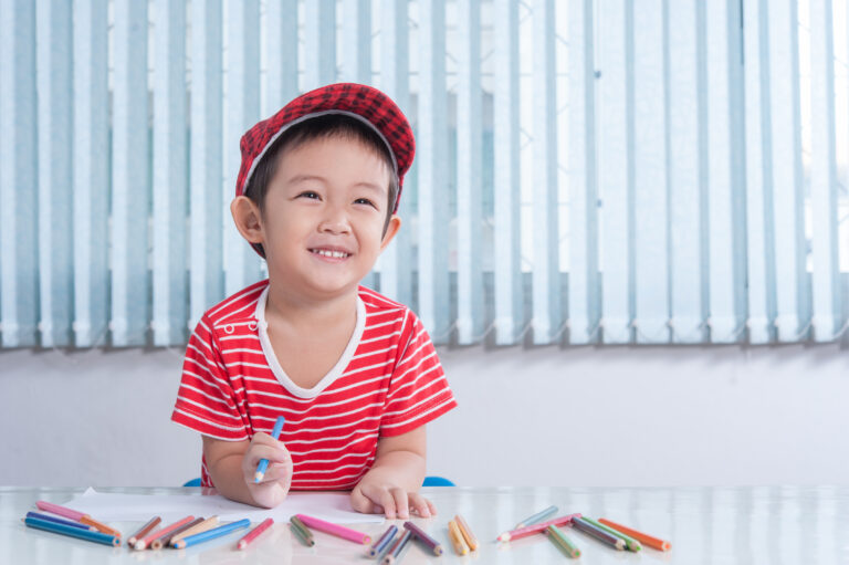 Cute boy draws with color pencils in the children's room Happy young child engaging in early intervention activities with colored pencils, highlighting the benefits of starting ABA-VB therapy early for autism