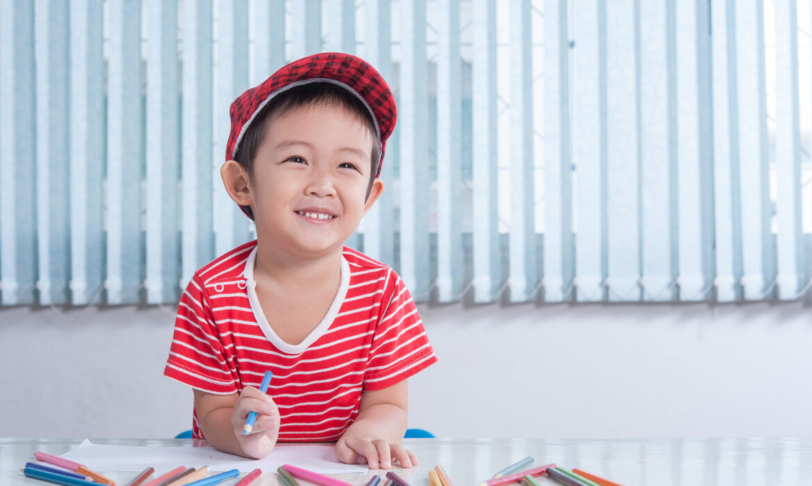 Happy young child engaging in early intervention activities with colored pencils, highlighting the benefits of starting ABA-VB therapy early for autism