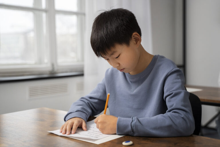 Unlocking Potential Through Psychological Assessments What They Offer And What’s Next Focused young boy completing a written test at a desk in a classroom, representing the role of psychological assessments in unlocking children's cognitive and academic potential.