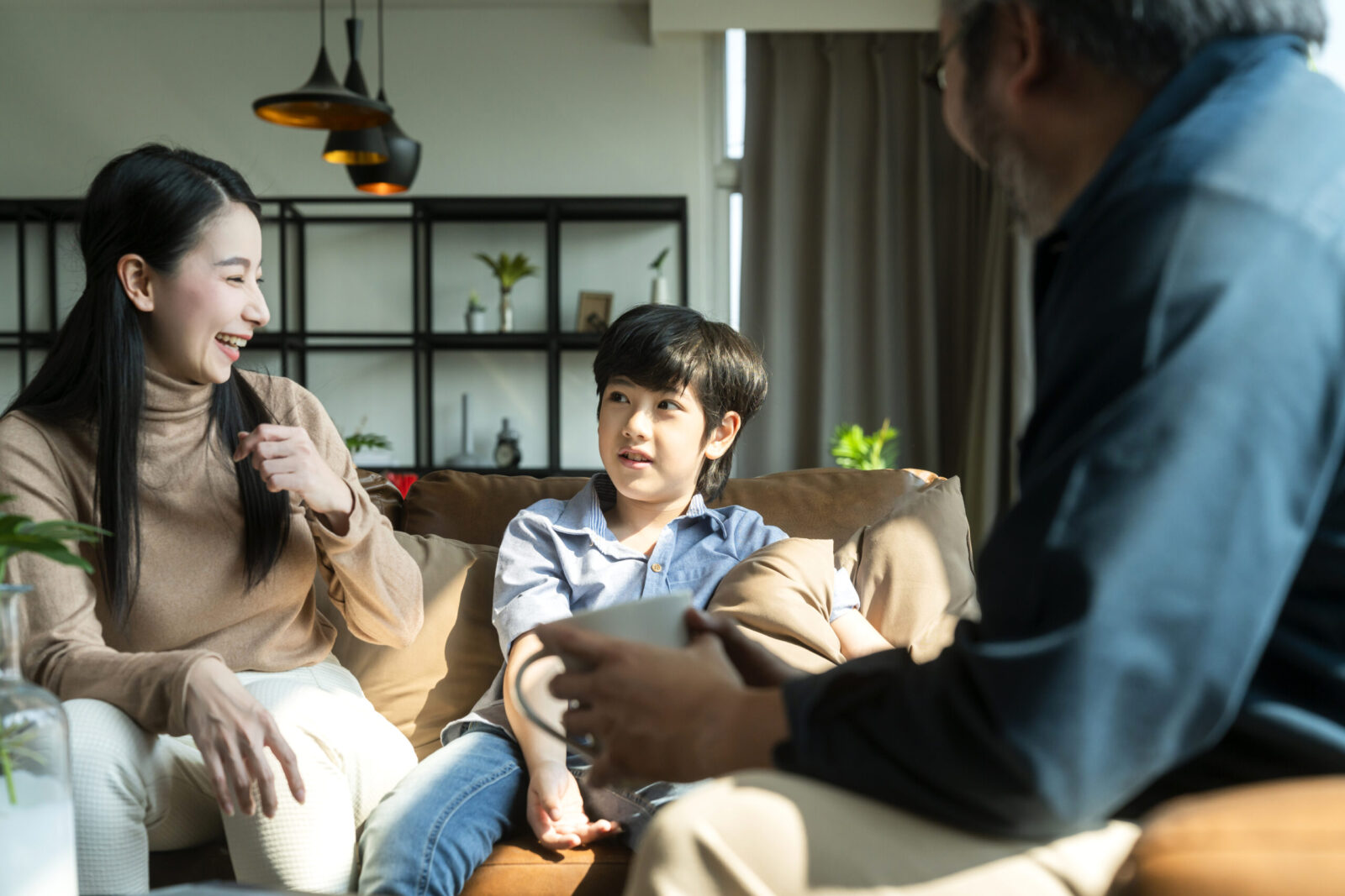 A mother and son engage in a warm conversation with a father figure in a cozy living room, illustrating a supportive and comfortable environment, which aligns with a parent’s experience during their first ABA-VB therapy session.