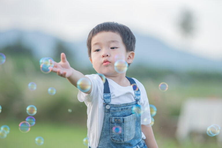 Children's Day. Little boy blowing soap bubbles in the park. cut Child engaging in playful bubble activity outdoors, illustrating integrating therapeutic strategies into everyday activities for children with autism.