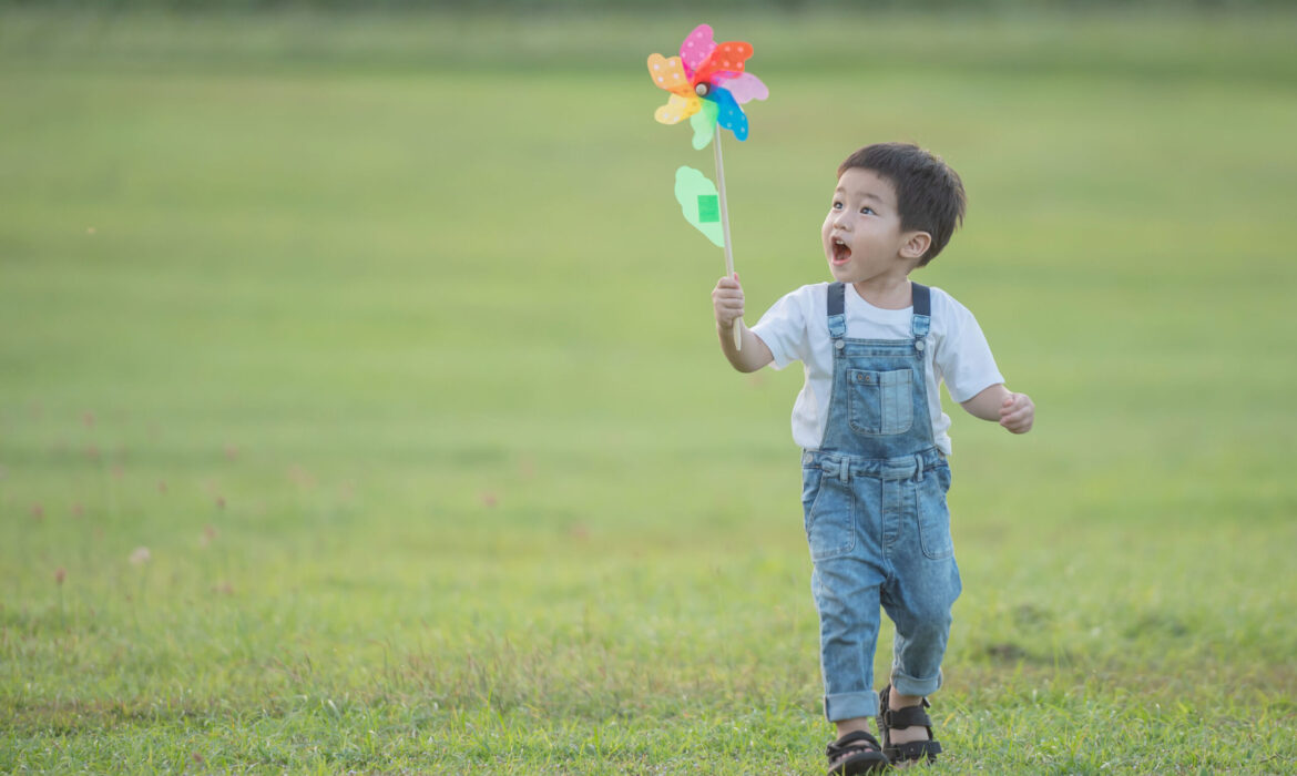 Toddler holding a colorful pinwheel while walking on grass, illustrating the difference between normal toddler behavior and early autism signs.