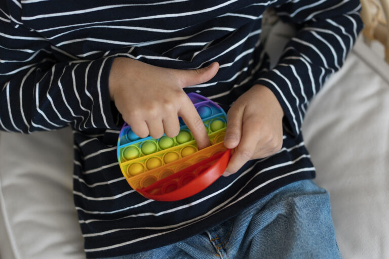 What Is Stimming Understanding Self-Stimulatory Behaviours In Children With Autism Child engaging in stimming behavior by playing with a rainbow-colored pop-it toy, illustrating self-stimulatory activity in autism.