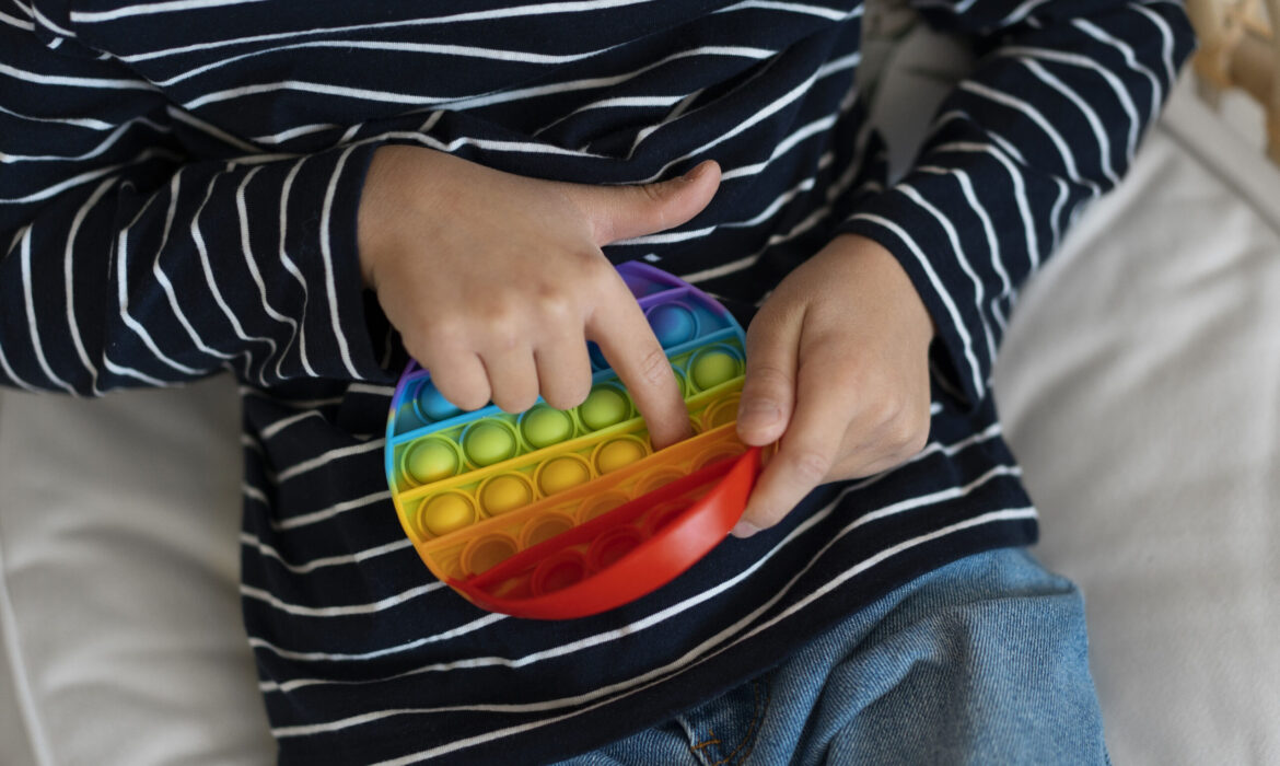 Child engaging in stimming behavior by playing with a rainbow-colored pop-it toy, illustrating self-stimulatory activity in autism.