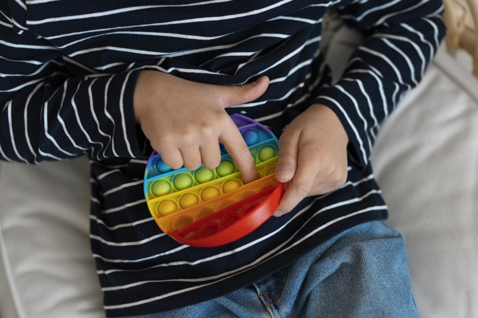 Child engaging in stimming behavior by playing with a rainbow-colored pop-it toy, illustrating self-stimulatory activity in autism.