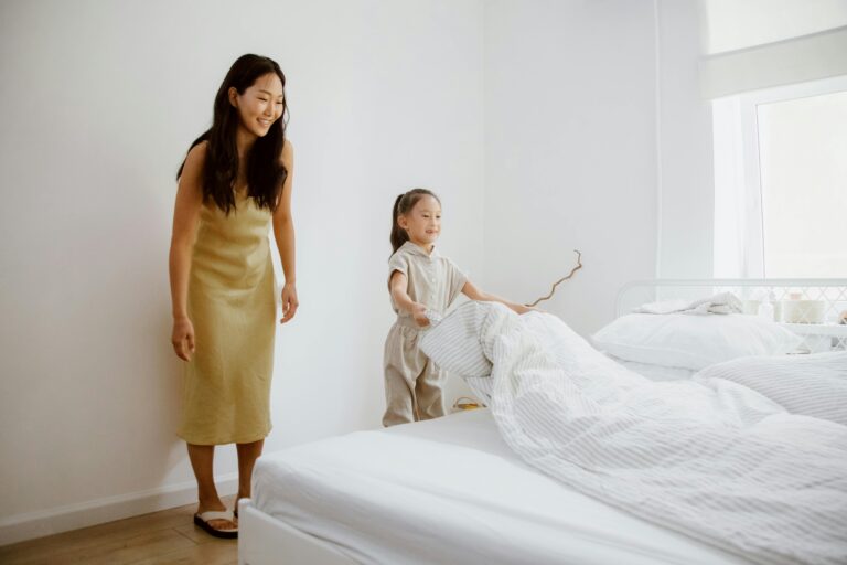 Transitioning Out Of Childhood Building Independence In Adolescents With Autism A mother helping her young daughter make the bed, symbolizing early steps toward building independence and life skills in adolescents with autism in a supportive home environment.