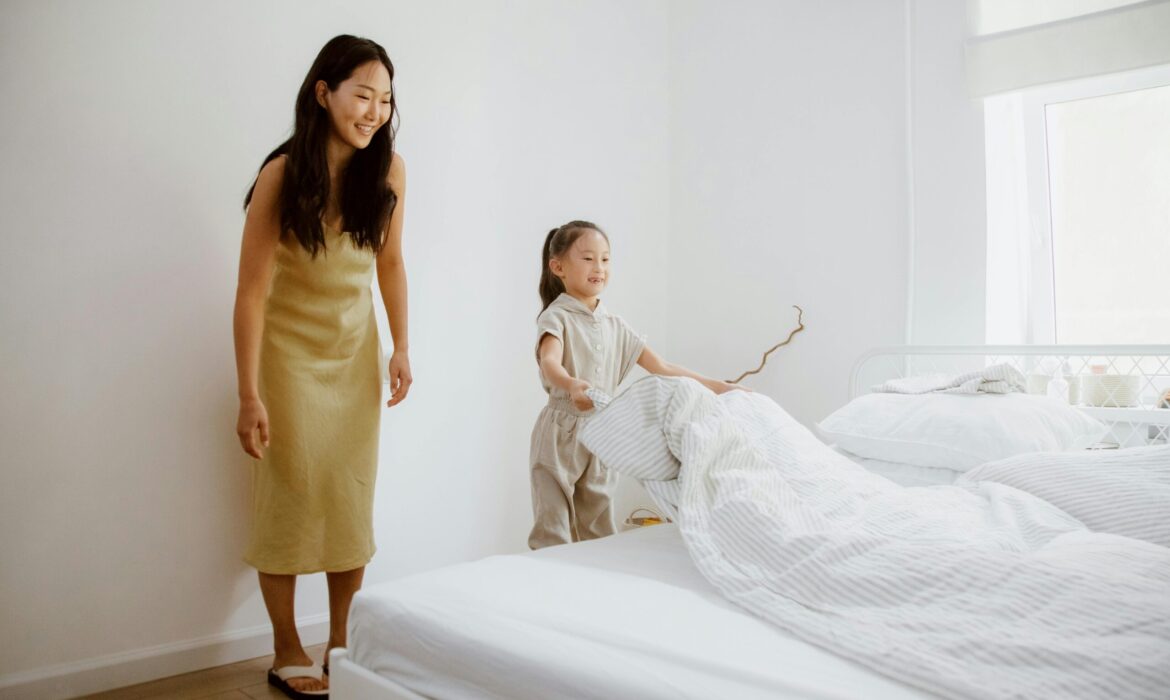 A mother helping her young daughter make the bed, symbolizing early steps toward building independence and life skills in adolescents with autism in a supportive home environment.