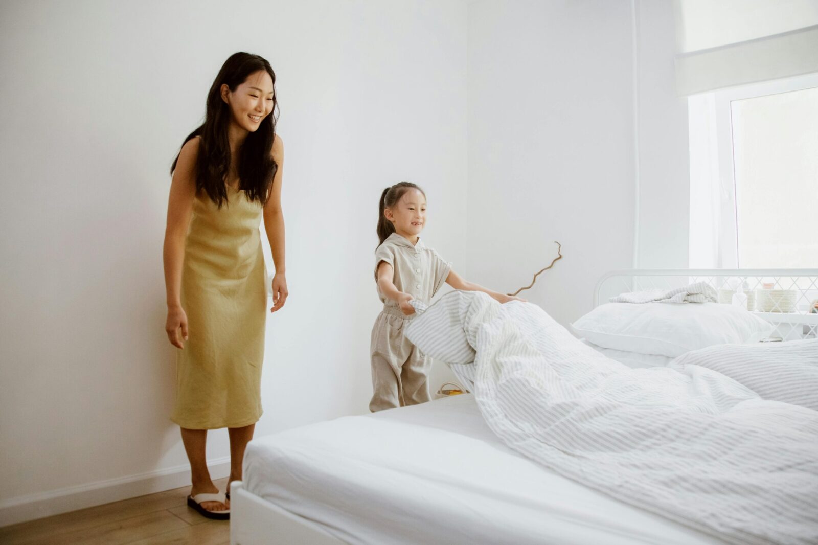 A mother helping her young daughter make the bed, symbolizing early steps toward building independence and life skills in adolescents with autism in a supportive home environment.