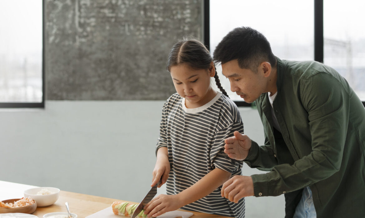 A father guides his daughter as she carefully cuts sushi rolls on a kitchen counter, illustrating hands-on learning and skill-building. A concept relevant to vocational training for teens with autism.