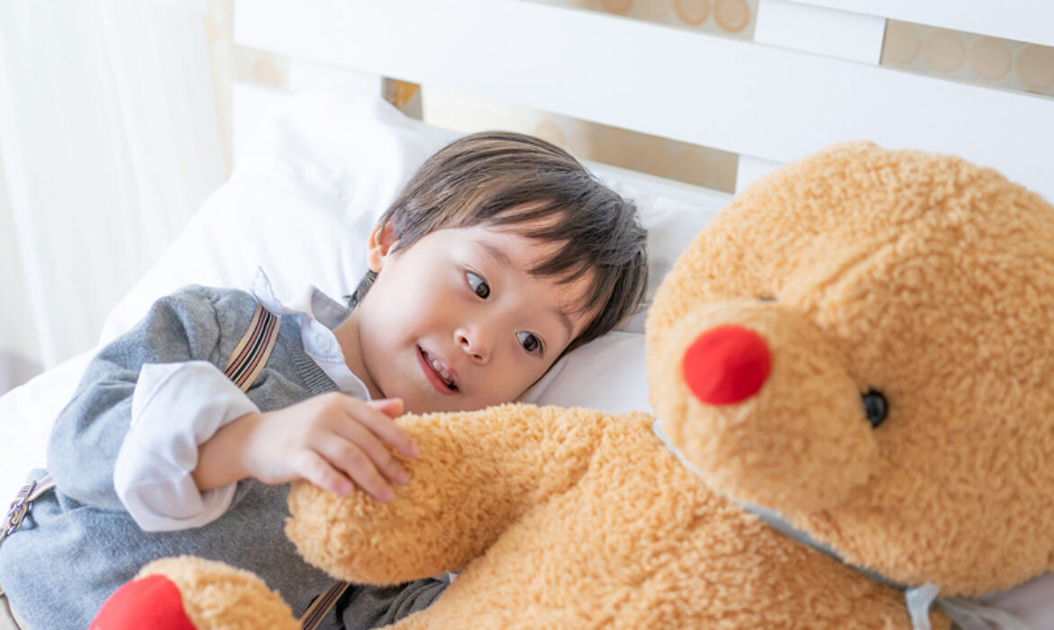 Young boy lying in bed interacting with a teddy bear.