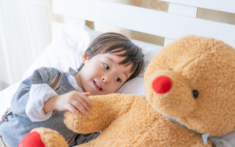 Young boy lying in bed interacting with a teddy bear.