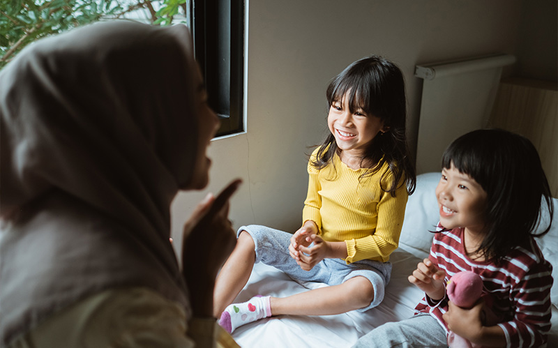 A mother in a hijab engaging her two young children in a verbal storytelling session.