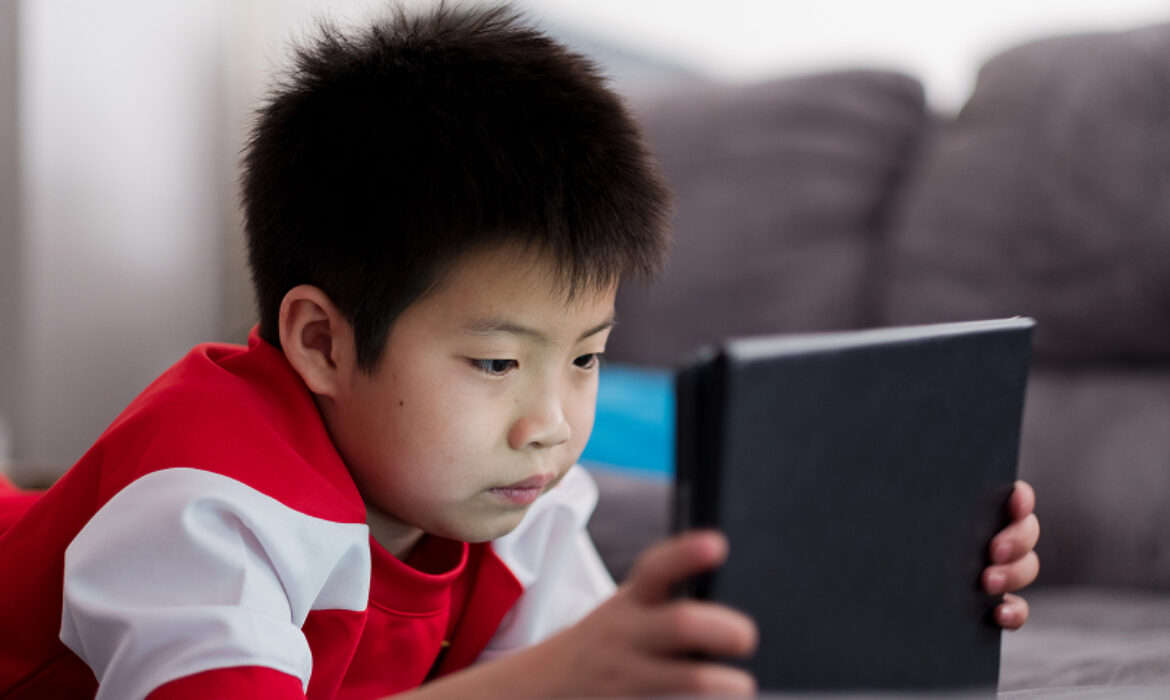 Young boy focused on using a tablet while lying down.