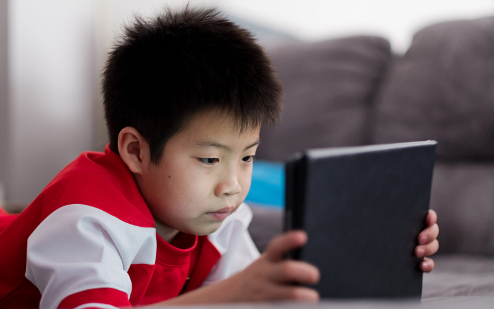 Young boy focused on using a tablet while lying down.
