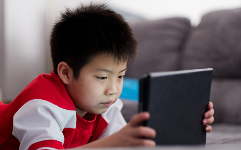 Young boy focused on using a tablet while lying down. Young boy focused on using a tablet while lying down.