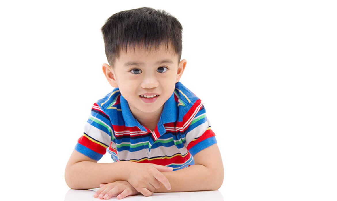 Child in striped polo leans on white surface.