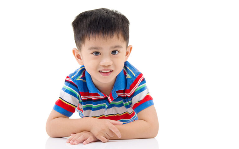 Child in striped polo leans on white surface.