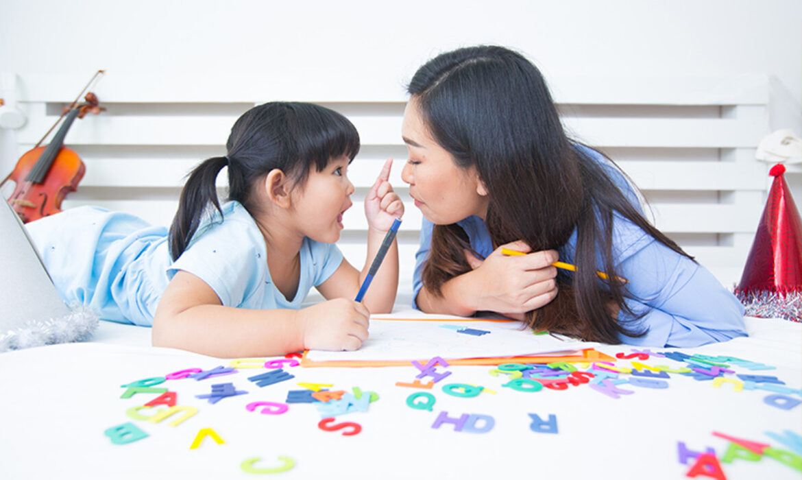 A mother and daughter lying on a bed with educational toys and alphabet letters