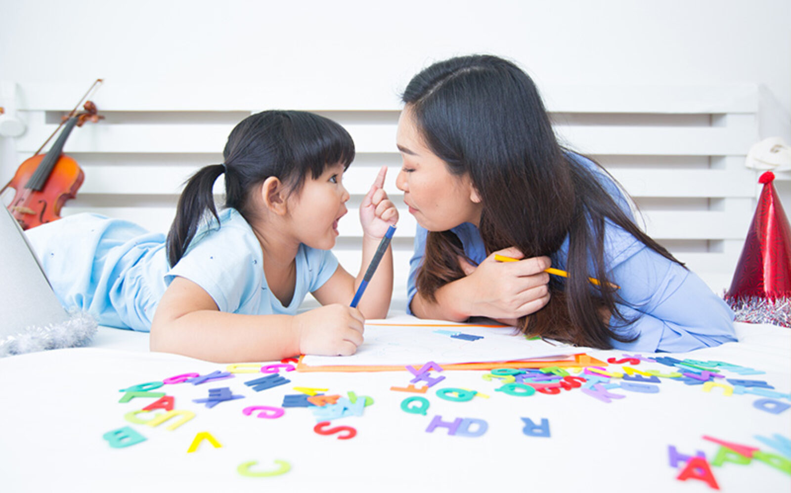 A mother and daughter lying on a bed with educational toys and alphabet letters