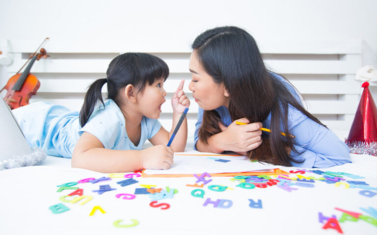 A mother and daughter lying on a bed with educational toys and alphabet letters