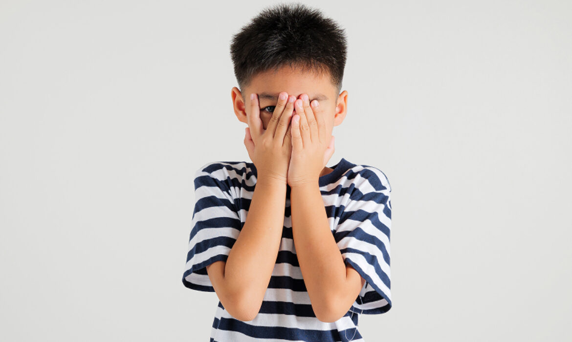 Child covering face with hands showing social anxiety or shyness.