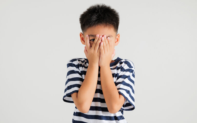 Child covering face with hands showing social anxiety or shyness.