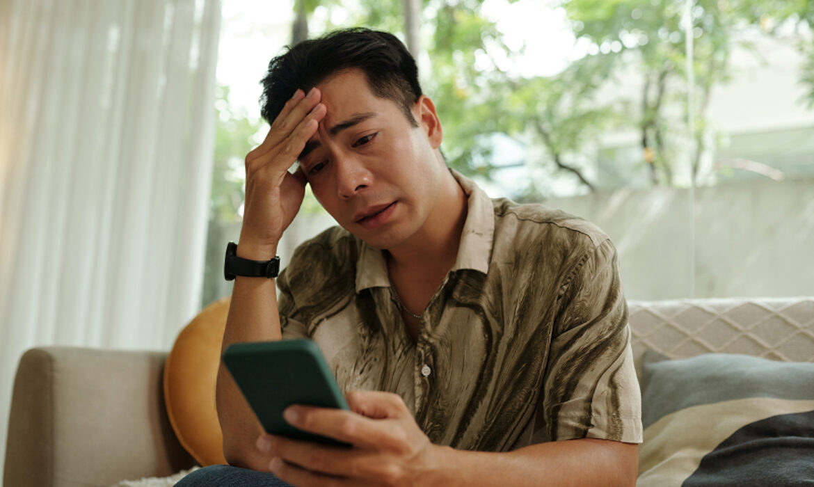 Concerned man looking at phone screen while sitting on sofa.