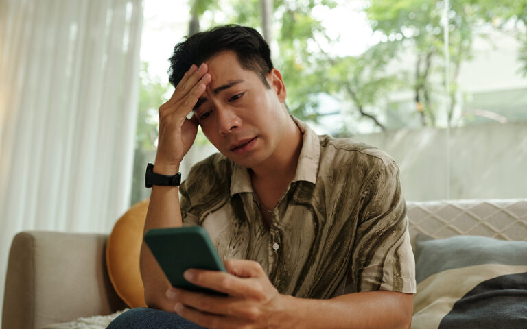 Concerned man looking at phone screen while sitting on sofa.